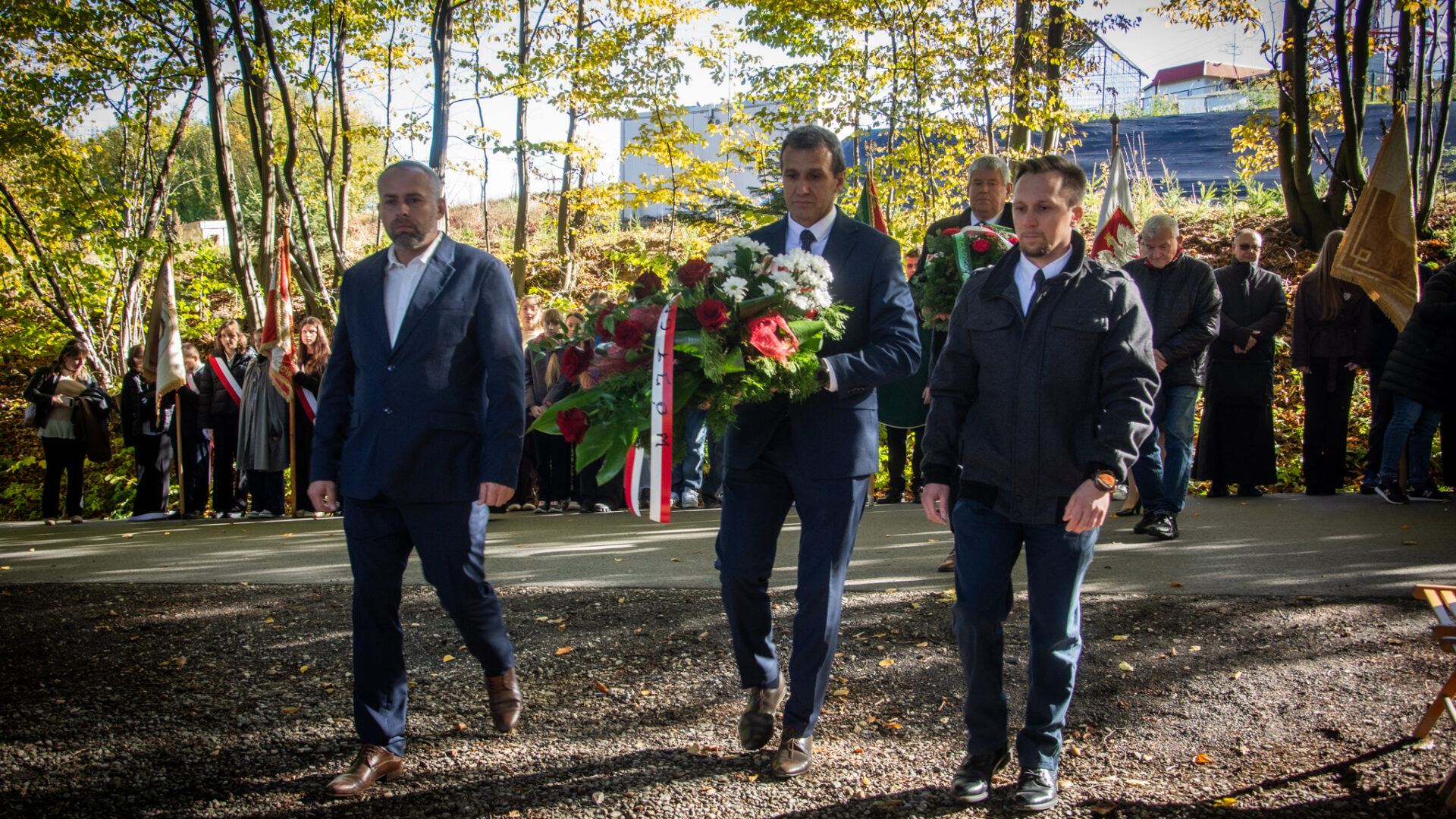 Delegacja trzech mężczyzn składa wiązankę kwiatów.